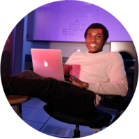 A male student leans back in an office chair with a laptop sitting on his lap.